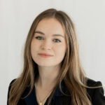 Headshot of Rachel Annichiarico, a young woman with long hair wearing a dark blazer over a blue collared shirt.