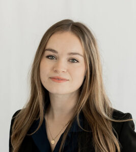 Headshot of Rachel Annichiarico, a young woman with long hair wearing a dark blazer over a blue collared shirt.