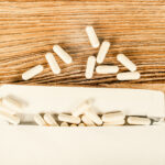 White capsules spilling from an open white paper package onto a wooden surface, with several capsules scattered above the package—an image evoking the ongoing debate over America’s abortion law.
