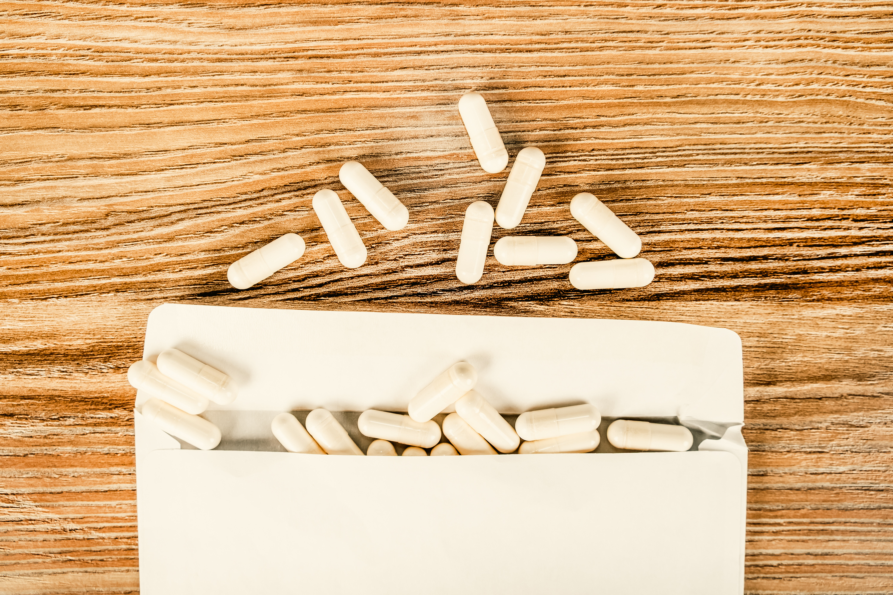 White capsules spilling from an open white paper package onto a wooden surface, with several capsules scattered above the package—an image evoking the ongoing debate over America’s abortion law.
