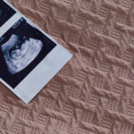 An orange pill bottle, scattered white pills, and an ultrasound photo strip rest on a textured pink fabric surface, symbolizing the experience of a medical abortion.
