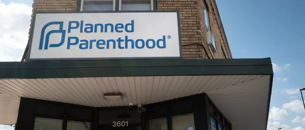 A sign displaying the Planned Parenthood logo and name is mounted above the entrance of a brick building