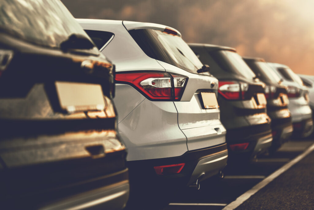 Row of parked American cars in a parking lot, photographed from the rear at sunset, with warm sunlight reflecting off the SUVs.