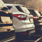 Row of parked American cars in a parking lot, photographed from the rear at sunset, with warm sunlight reflecting off the SUVs.