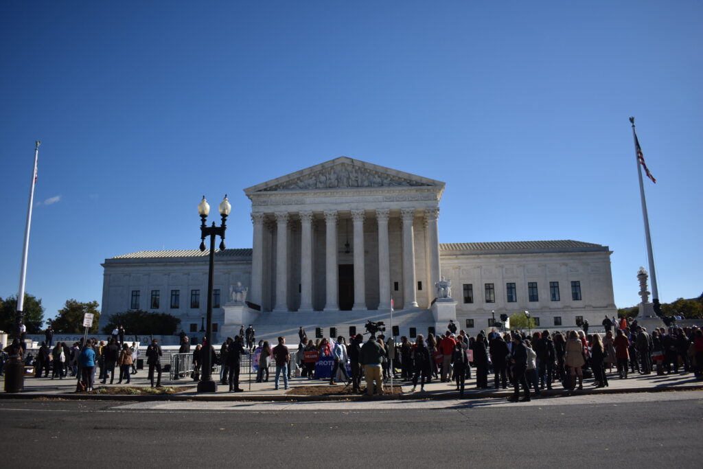 A large crowd gathers in front of the U.S. Supreme Court building in Washington, D.C., under a clear blue sky, as discussions on trends and the Dobbs decision unfold amid visible columns and flags.