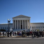 A large crowd gathers in front of the U.S. Supreme Court building in Washington, D.C., under a clear blue sky, as discussions on trends and the Dobbs decision unfold amid visible columns and flags.