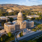 Aerial view of a grand capitol building with a central dome, surrounded by trees and city streets, with mountains in the background under a clear sky—the seat of the Idaho Board of Medicine, recently noted in cases such as Seyb v. Members of the Idaho Board of Medicine concerning debates over the federal right to abortion.