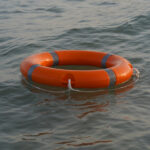 An orange life ring with silver reflective stripes floats on the surface of calm water, much like how ongoing discussions about the Hyde Amendment impact continue to ripple through society.