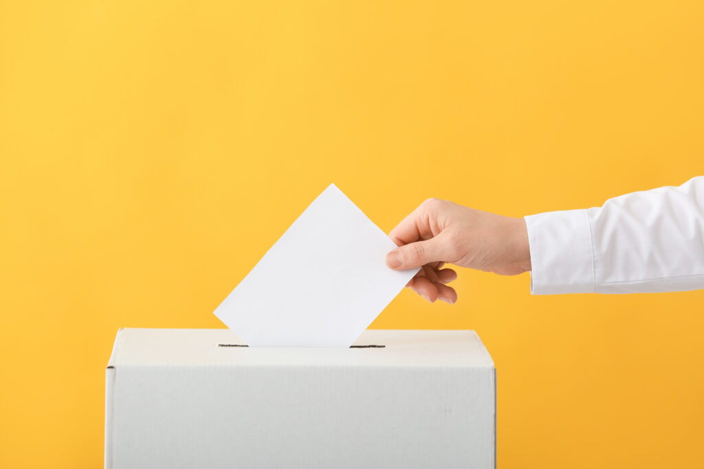 A person in a white shirt dropping an abortion ballot into a white box against a yellow background.