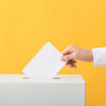 A person in a white shirt dropping an abortion ballot into a white box against a yellow background.