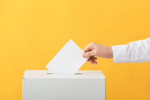 A person in a white shirt dropping an abortion ballot into a white box against a yellow background.