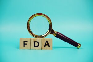 A magnifying glass rests on three wooden blocks that spell out FDA, symbolizing a review of the REMS modification.