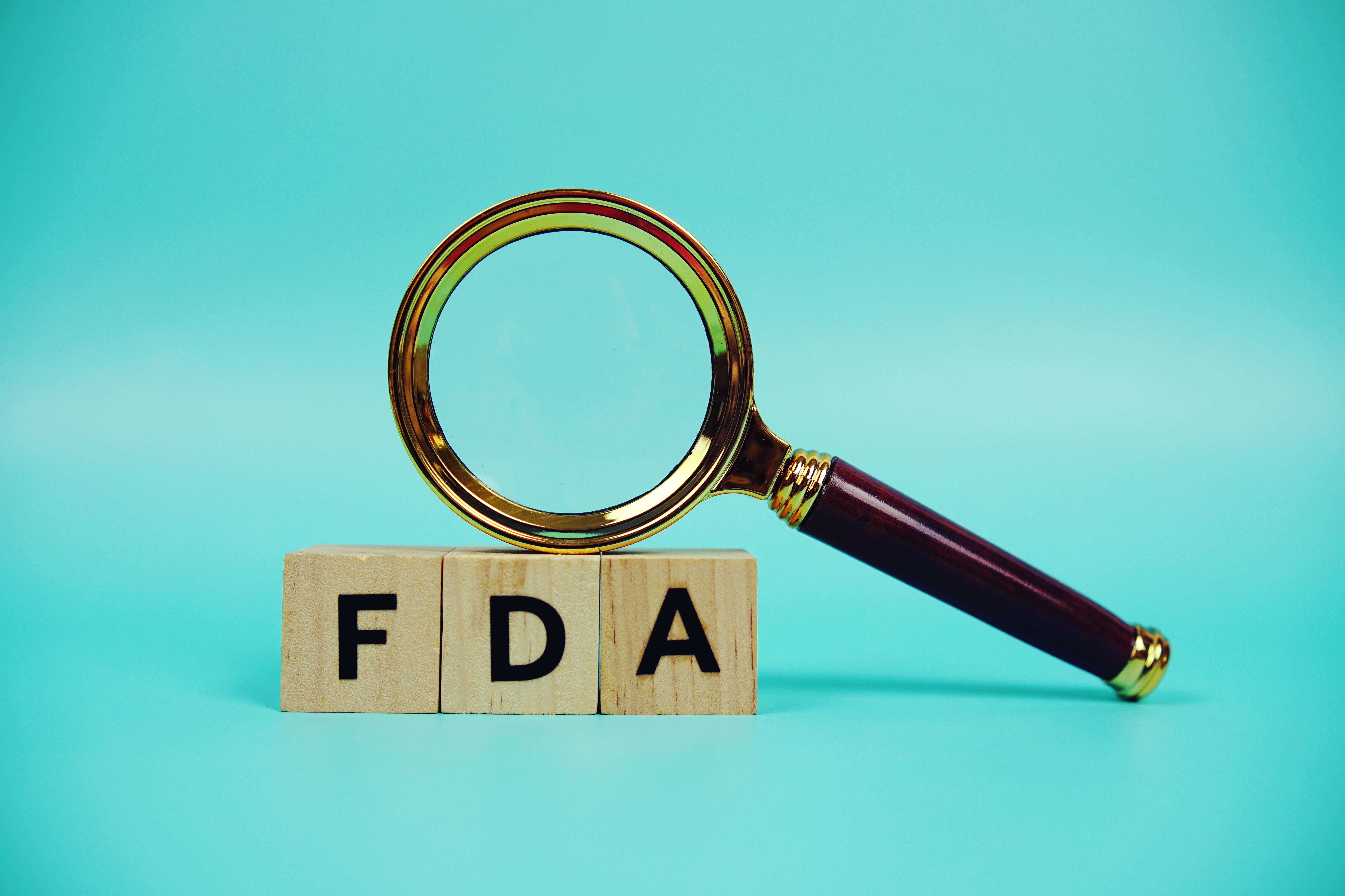 A magnifying glass rests on three wooden blocks that spell out FDA, symbolizing a review of the REMS modification.